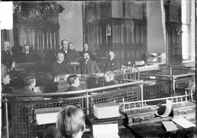 ECC | [Men at the speaker's rostrum of the Council Chamber during
